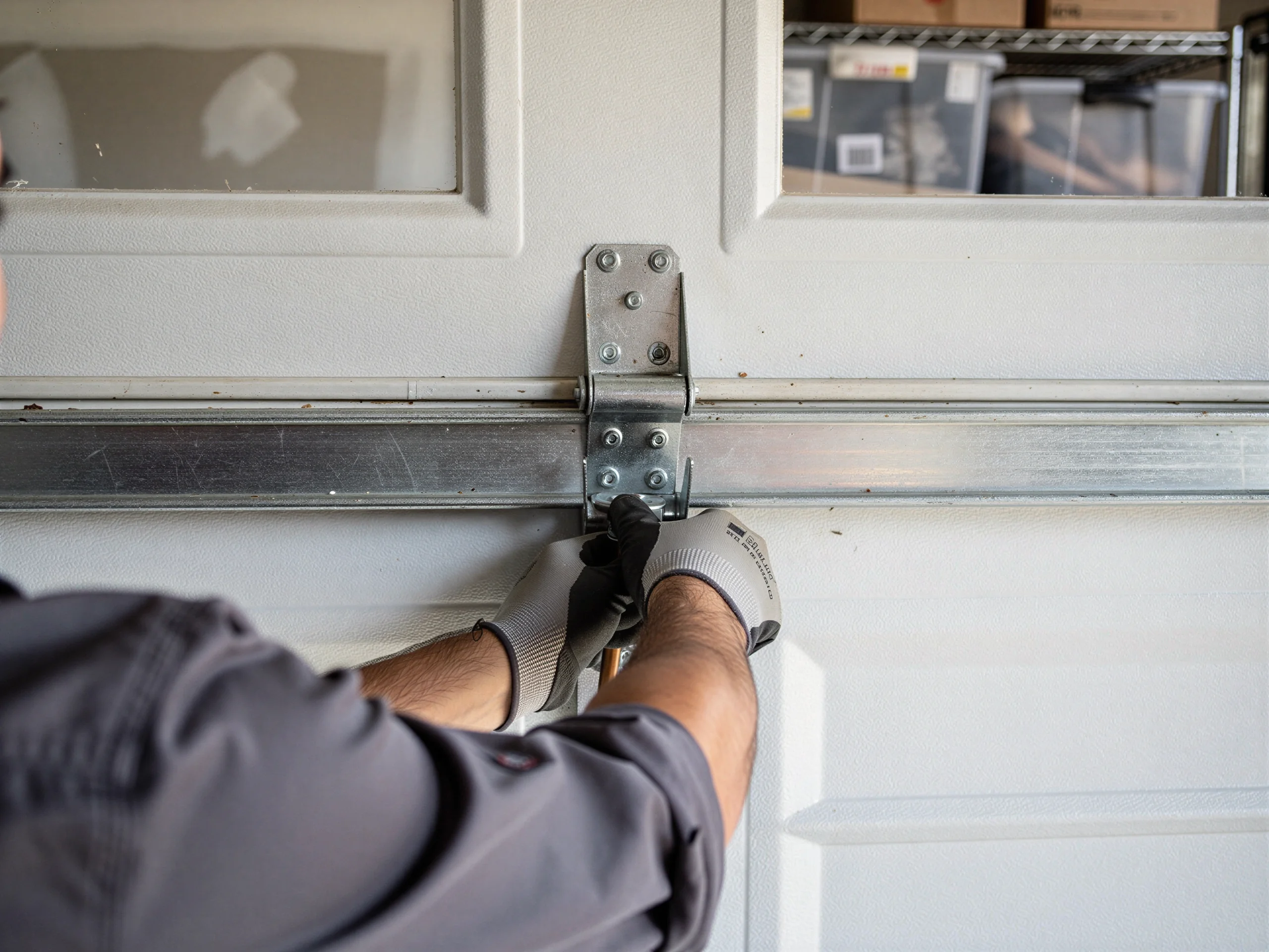 A technician in gloves works on a garage door hinge and roller.